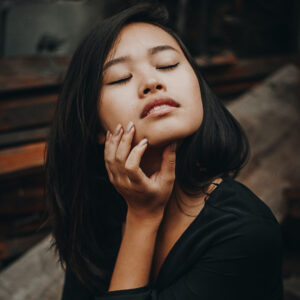 Woman with eyes closed bends face upward with hand on jaw. 