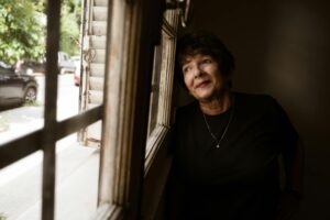 Older woman leaning next to window and looking out thoutfully.