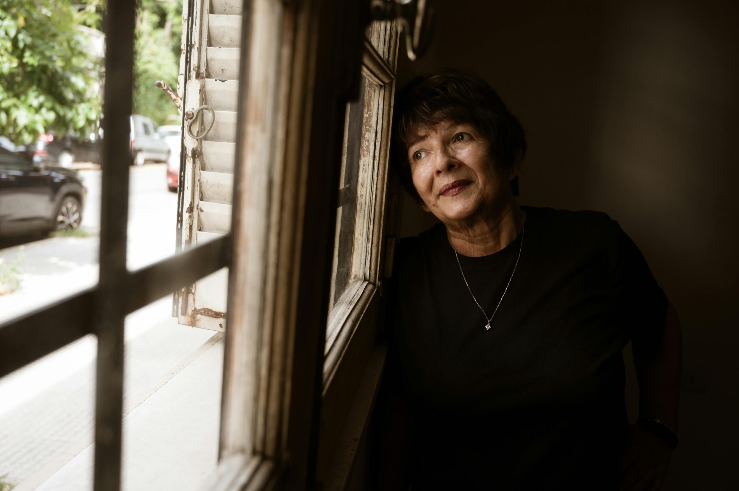 Older woman leaning next to window and looking out thoutfully.