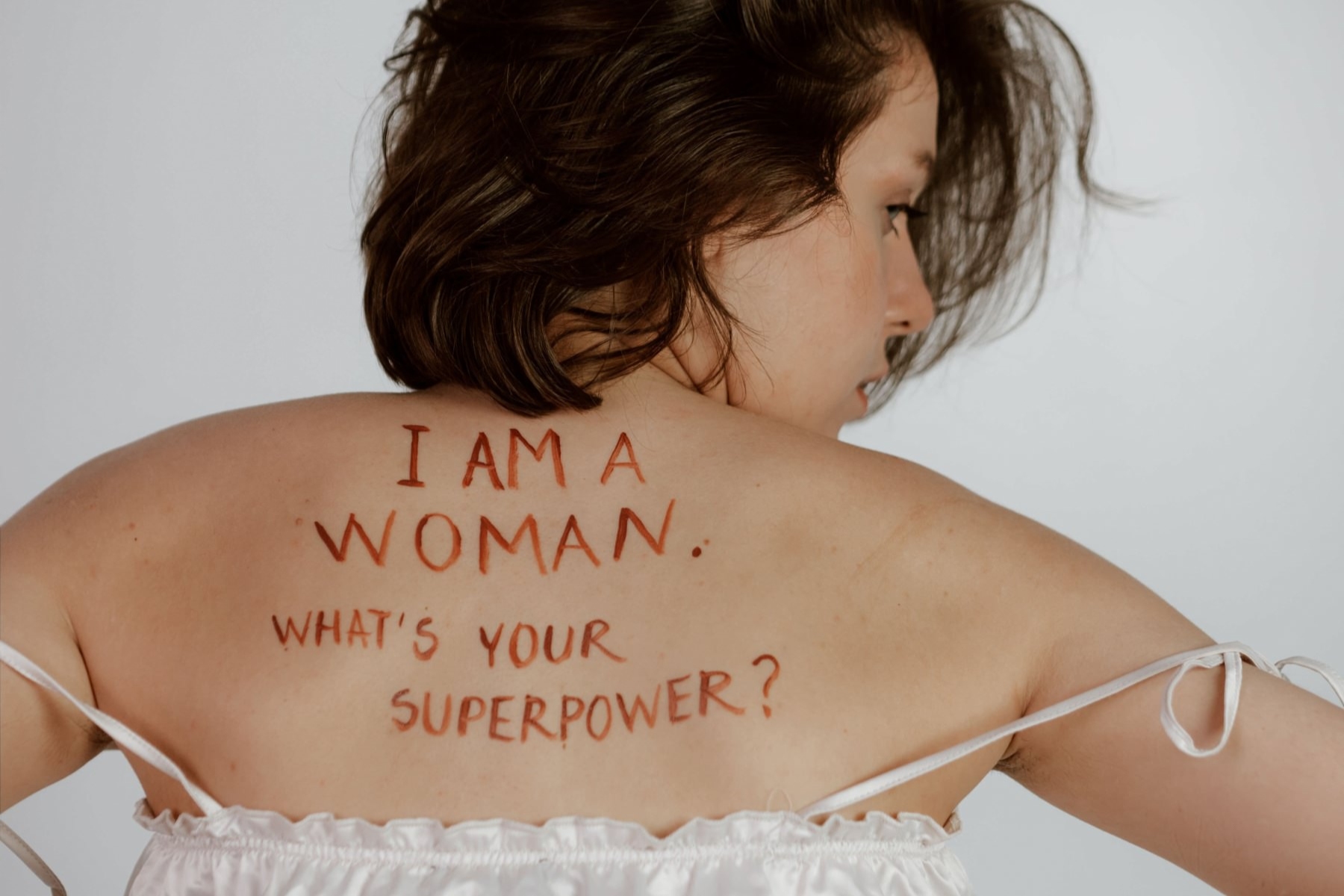 A woman has her back to the camera and written on her back it says, "I am Woman. What's your super power?"