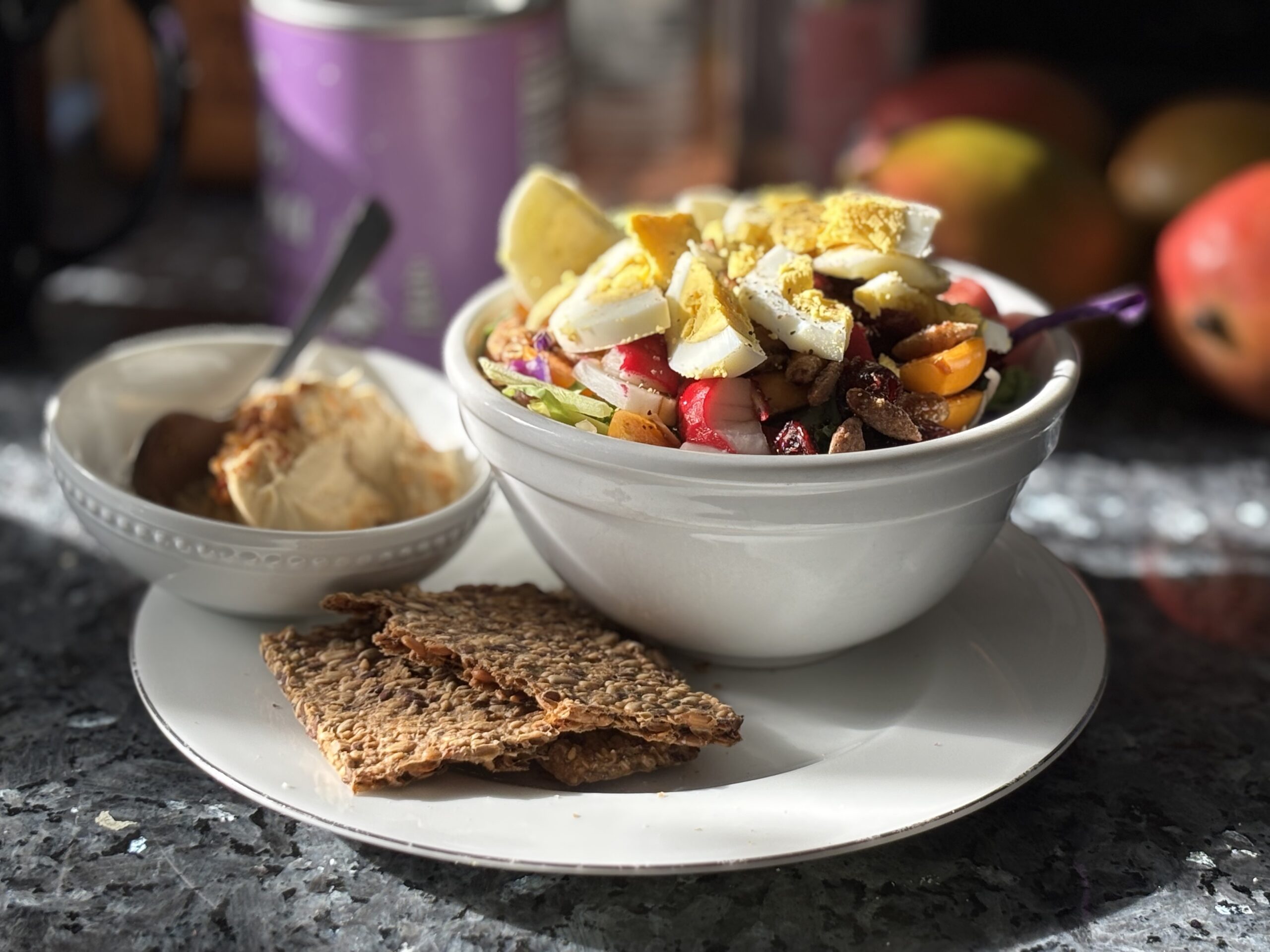 Healthy lunch of salad topped with eggs, a side of hummus with gluten free crackers on a plate.
