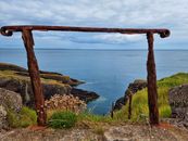 Rusty iron frame overlooking serene rocky coastline and expansive sea view.